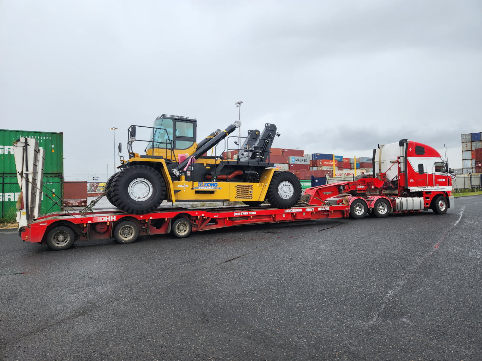 DHH truck carrying yellow XCMG machinery beside shipping containers